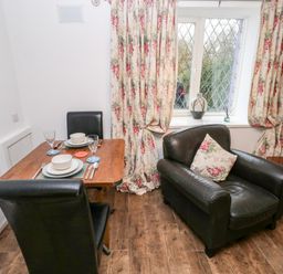 A dining table set for two with black chairs next to a black armchair and window with floral curtains at The Coach House in St Florence