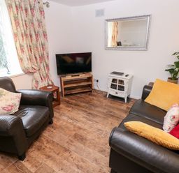 A living room with leather armchairs a television on a wooden stand floral curtains and cushions at The Coach House in St Florence