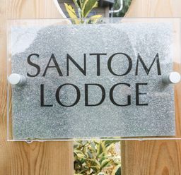 A sign with the text santom lodge on a wooden surface with plants behind it at Coniston View 9 Dock Acres near Tewitfield