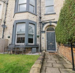 The exterior of a brick house with a gray door and bay windows a paved walkway and a green hedge at Westbourne House in Scarborough