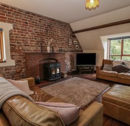A living room with leather sofas a brick wall with a fireplace and windows at Owlbury Hall Barn in Snead near Bishops Castle Montgomery