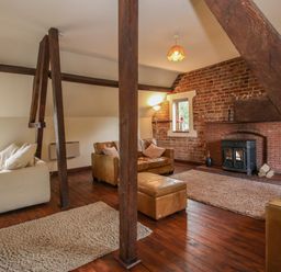 A living room with wooden beams leather sofas a fireplace and rugs at Owlbury Hall Barn in Snead near Bishops Castle Montgomery