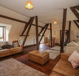 A living room with wooden beams brown leather sofas beige rugs and a dining table at Owlbury Hall Barn in Snead near Bishops Castle Montgomery