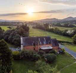 A countryside house with a glass conservatory surrounded by greenery and a driveway at Owlbury Hall Barn in Snead near Bishops Castle Montgomery