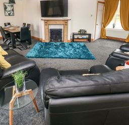 A living room with black leather sofas a blue rug a wooden fireplace and a dining table with chairs at Ocean House in Broad Haven