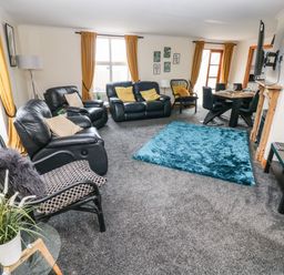 A living room with black leather sofas a blue rug a dining table and mustard curtains at Ocean House in Broad Haven