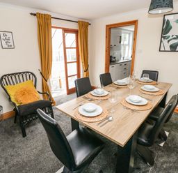 A dining room with a wooden table set for six and black chairs at Ocean House in Broad Haven