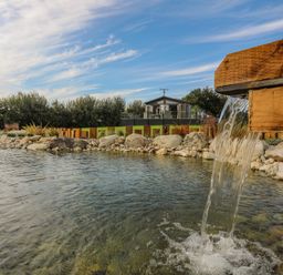 A wooden water spout flowing into a pond with rocks and a house in the background at Fairview Lodge in Pwllheli