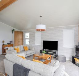 A living room with two sofas a wooden coffee table a television and a wood stove at Fairview Lodge in Pwllheli