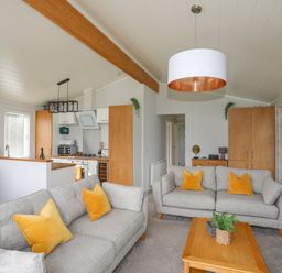A living room with two gray sofas and yellow cushions a wooden coffee table and kitchen area at Fairview Lodge in Pwllheli