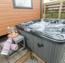 An outdoor hot tub with bubbling water next to a wooden wall with a small wooden bench holding a towel and a tray with champagne and glasses at Starfish Retreat in Little Haven near Broad Haven