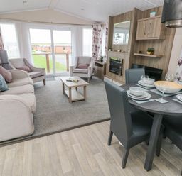 A living room with a sofa, armchairs, coffee table, dining table with chairs and tableware at Starfish Retreat in Little Haven near Broad Haven