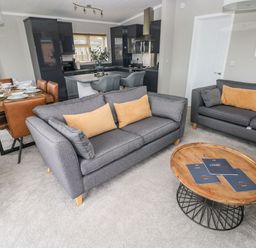 A living room with two grey sofas, a wooden coffee table, and a dining table with brown chairs next to a kitchen at Driftwood Lodge in Hasguard Cross near Broad Haven
