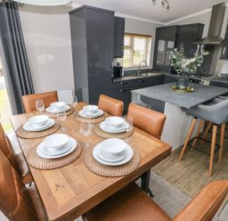 A dining area with leather chairs and place settings next to a kitchen with gray cabinets and a breakfast bar at Driftwood Lodge in Hasguard Cross near Broad Haven