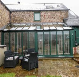 A stone house with a glass conservatory and outdoor seating at Skomer Cottage Sandy Haven near Milford Haven