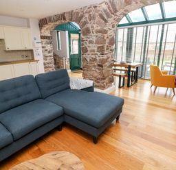 A living room with a blue sectional sofa exposed stone arches and a dining area with yellow chairs at Skomer Cottage in Sandy Haven near Milford Haven