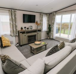 A living room with beige sofas a wooden coffee table a wall-mounted television and large windows at Ramsey in Broad Haven