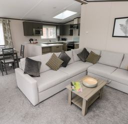 A living room with a gray sectional sofa and coffee table connected to a kitchen and dining area at Ramsey in Broad Haven