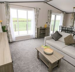 A living room with a sofa coffee table and dining area with large windows and curtains at Ramsey in Broad Haven