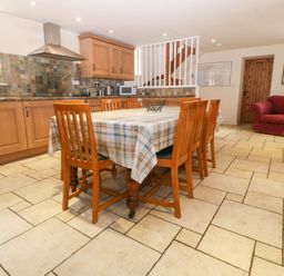 A kitchen dining area with a wooden table and six chairs a red armchair and wooden cabinets at Tyn Llwyn in Eisingrug near Harlech