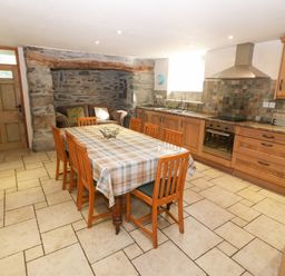 A kitchen with wooden cabinets a dining table with chairs and a stone wall at Tyn Llwyn in Eisingrug near Harlech