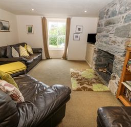 A living room with leather sofas a stone fireplace a bookshelf and a window with curtains at Tyn Llwyn in Eisingrug near Harlech