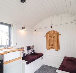 A small white kitchen and seating area with a window and wooden folding table at Shepherds Hut in Dunvegan
