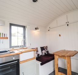 A small kitchen and dining area with a stove sink wooden table and cushioned benches at Shepherds Hut in Dunvegan