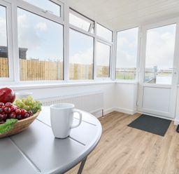 A room with large windows wooden floor a table with a bowl of fruit and two white mugs at Cliff Barn in Burton Bradstock