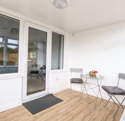 A small indoor seating area with two chairs and a round table with fruit bowl near a glass door at Cliff Barn in Burton Bradstock