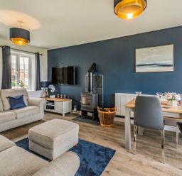 A living room with a beige sofa and ottoman a wood stove a dining table with chairs and a wall-mounted TV at Lantern House in Filey