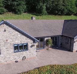 Stone house with tiled roof and windows overlooking a paved patio with grass and trees behind at Pen Y Banc in Llanfaredd near Builth Wells