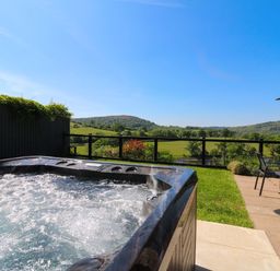 An outdoor patio with a bubbling hot tub table and chairs overlooking green hills and fields at Pen Y Banc in Llanfaredd near Builth Wells