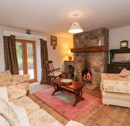 A living room with a stone fireplace a wooden coffee table patterned sofas a rocking chair and glass doors leading outside at Coffey's in Ballymacarbry County Waterford