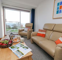 A living room with beige leather sofas and a wooden coffee table with fruit and tea set by a window with a sea view at Kiama in Weymouth