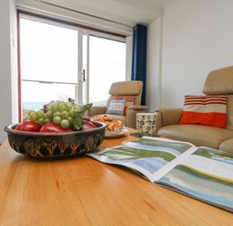 A living room with a wooden table holding a bowl of fruit a magazine and a cup in front of two leather armchairs with striped cushions at Kiama in Weymouth