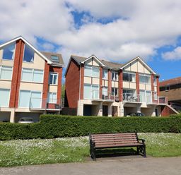 A bench on grassy area in front of residential buildings with balconies and parked cars at Kiama in Weymouth