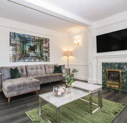 A living room with a gray sofa green rug and a fireplace with a TV above at Alcombe House in Minehead
