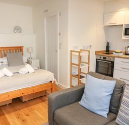 A studio apartment with a wooden bed and gray sofa near a small kitchen area at The Mew in Dartmouth
