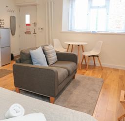A small living space with a gray sofa two white chairs and table near a window and a small kitchen area at The Mew in Dartmouth