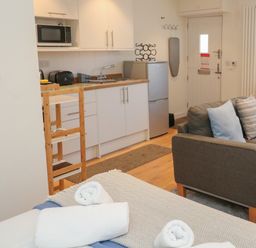 A studio apartment with a kitchen area a grey sofa and a bed with rolled towels at The Mew in Dartmouth