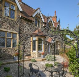A stone house with leaded glass windows and a small garden seating area at Gable Lodge in Malvern