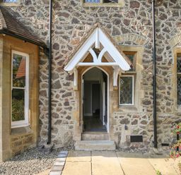 A stone exterior wall with a small arched doorway and three windows at Gable Lodge Malvern
