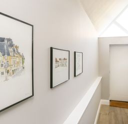 A hallway with three framed paintings on the wall a white door and a brown doormat at Gable Lodge in Malvern