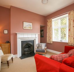 A living room with a fireplace a red sofa a gray chair and a white chair near a window at Gable Lodge in Malvern