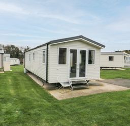 Several beige mobile homes on a grassy plot with one mobile home in the center with a white chair outside at Pines 30 in Cayton