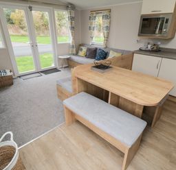 An open plan kitchen and living area with a wooden dining table bench and sofa near windows and glass doors at Pines 30 in Cayton