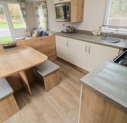 A kitchen area with a wooden dining table and benches a sink stove microwave and sitting area at Pines 30 in Cayton