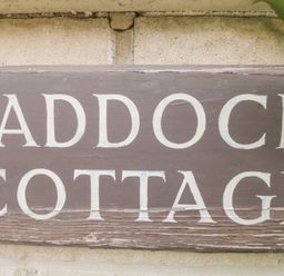 A close up of a wooden sign with the words Paddock Cottage on a wall at Paddock Cottage Nr Malmesbury