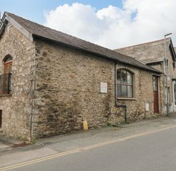 An old stone building with windows and doors along a paved road at Coach House in Arnside